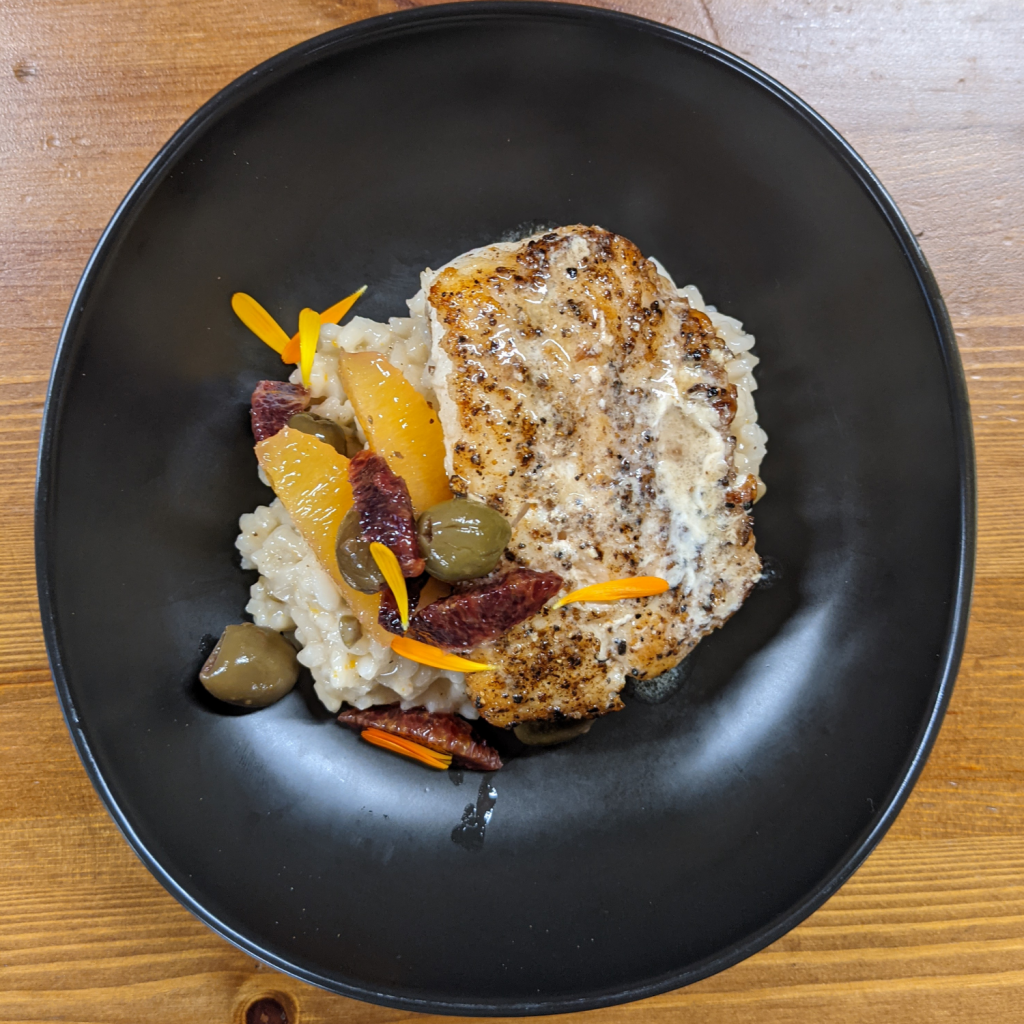 Spice crusted Lingcod on a bed of risotto with olives, and orange slices.
